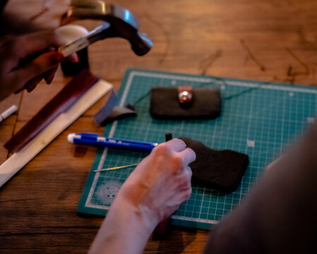 Female hand working on the leather wallet in her workshop. Working process with a brown natural leather. Craftsman holding a crafting tools