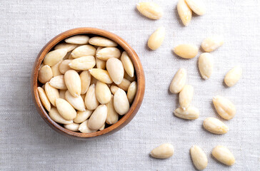 Freshly blanched almonds in a wooden bowl on linen. Shelled almonds that have been treated with hot water to soften the seed coat, which is then removed to reveal the seed. Fruits of Prunus amygdalus.