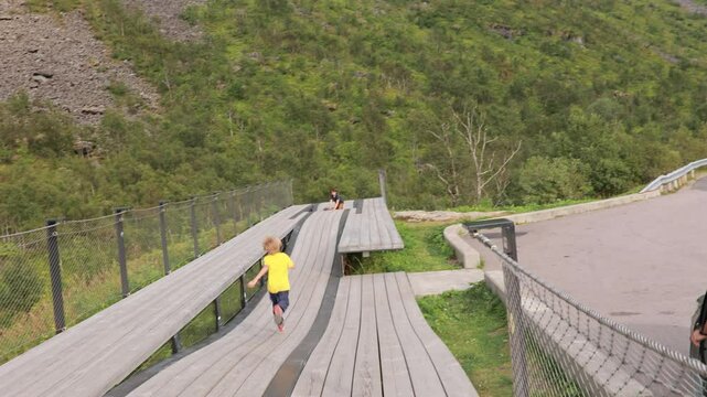 Children, standing on the edge of a 44 meter long viewing platform, overlooking the water of Bergsfjord, enjoying the view on Senja island, Norway
