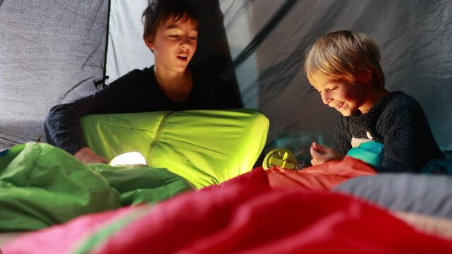Children, siblings, enjoying a night in a tent in camping, laughing and reading books