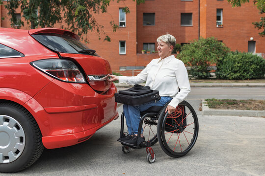 Woman with disability on wheelchair opening the trunk of her car to put the laptop before driving to work. Independency concept.