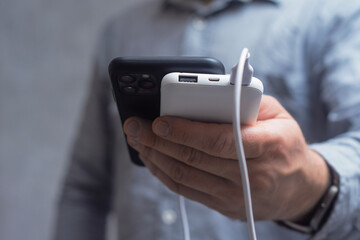 Man in a shirt holding a Smartphone and Power Bank against a gray concrete wall. A portable charger for gadgets.