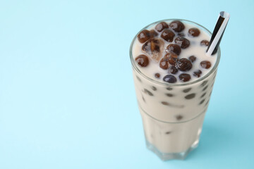 Tasty milk bubble tea in glass on light blue background, closeup. Space for text