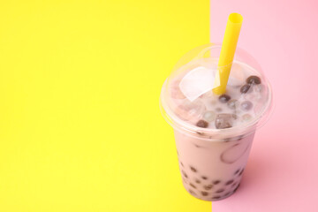 Tasty milk bubble tea in plastic cup on color background, space for text