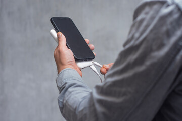 Man in a shirt holding a Smartphone and Power Bank against a gray concrete wall. A portable charger for gadgets.