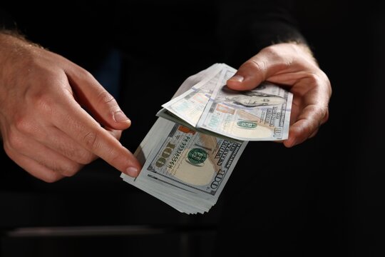 Corruption concept. Man holding dollar banknotes on black background, closeup