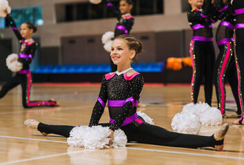 Beautiful teenage girl, professional cheerleader, gymnast acrobat with white pompoms in hands dancing in gym, sitting on splits. Photography, portrait, sport concept, cheerleading.