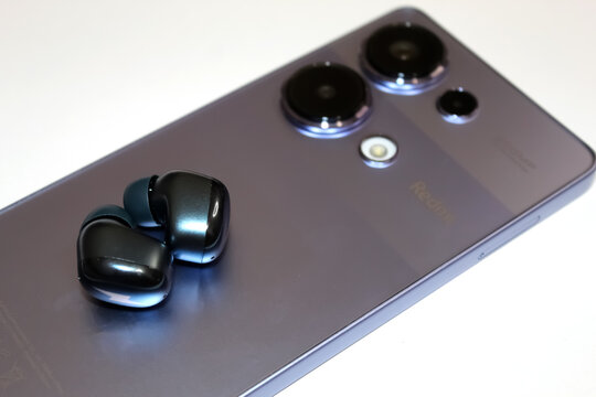 Kyiv, Ukraine. 10.10.2024: Wireless earbuds resting on a sleek smartphone Xiaomi redmi note 13 Pro and Redmi Buds 4 on a clean surface. Stock editorial photo.