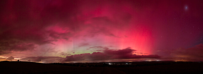 Aurora borealis in Saxony, Germany in the night of the 10. and 11. October 2024. Vibrant glowing northern lights visible at latitude 51 degrees north. Landscape at night with a cloudy sky.