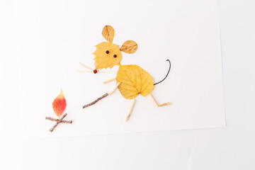 Mouse made of yellow autumn leaves standing near a campfire. Minimalistic flat lay composition with copy space. Autumn camping and nature craft concept for design and print