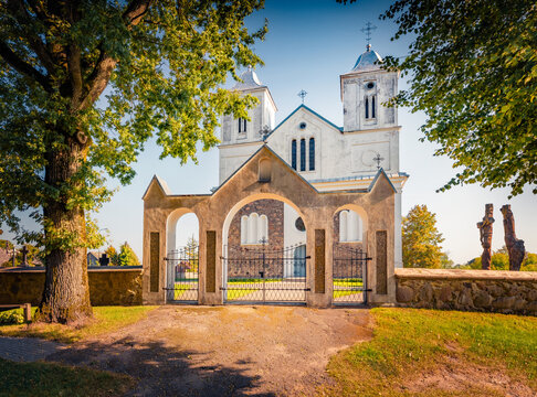 Sunny summer view of Catholic John the Baptist Church with three wooden sculptures. Stunning morning scene of Vainutas town, Silute District, Lithuania, Europe. Traveling concept background.