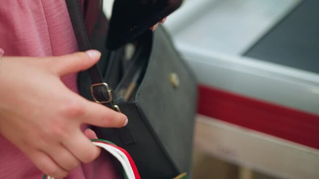 Hand view of lady searching through her handbag to retrieve her phone, followed by taking out a lemon-colored card, with a partial view of her shopping bag in her hand with a blurred surrounding
