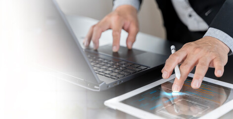 Businessman working on laptop, using mobile phone at modern office, analyzing business document with financial graph.
