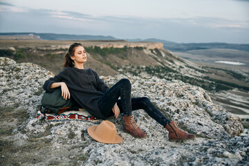 Serene woman enjoying the view from a mountain summit with backpack and hat nearby