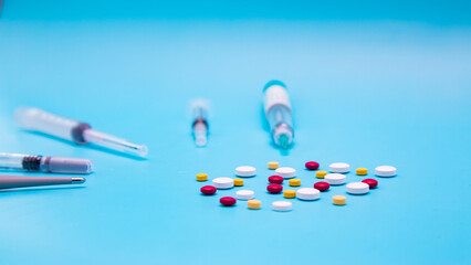 Colorful pills scattered on blue background with blurred syringes and thermometer. Idea for medicine, pharmacy, pharmaceutical, healthcare, medical treatment.