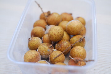 Frozen longan fruits in plastic container on wooden table. Selective focus.