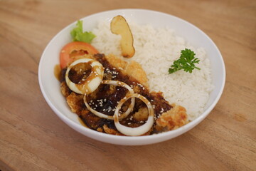 Rice with fried chicken and onion in white plate on wooden table