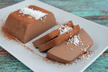 Dark chocolate milk pudding cake with cocoa powder and coconut flakes topping served on a plate. Selective focus