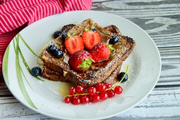 French toast crowned with vibrant strawberries, Red currant, blueberries and a fresh mint leaf, served with maple syrup, dusted delicately with powdered sugar
