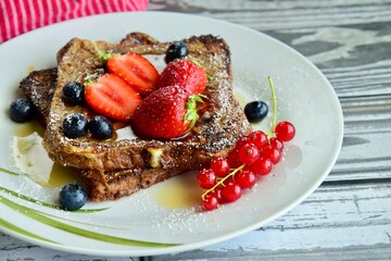 French toast crowned with vibrant strawberries, Red currant, blueberries and a fresh mint leaf, served with maple syrup, dusted delicately with powdered sugar