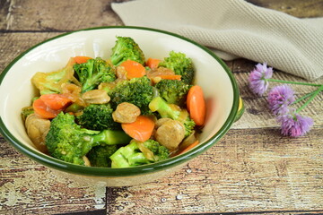 Stir fried broccoli with carrot and chicken sausage in a ceramic dish on wooden table. homemade style food concept.