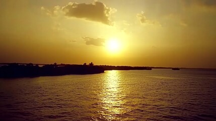 Naklejka premium A breathtaking golden sunset over a calm, reflecting river, with a silhouette of trees and a bridge in the distance.