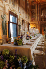 Modern luxury destination wedding decor in dark gold mode in historical Italian villa Arvedi with candelabras, gold chairs flowers and artworks