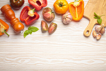 Colorful vegetables, a pepper mill, and a cutting board are filling the top of a white wooden tabletop frame. The arrangement leaves an empty space on the bottom for text or design