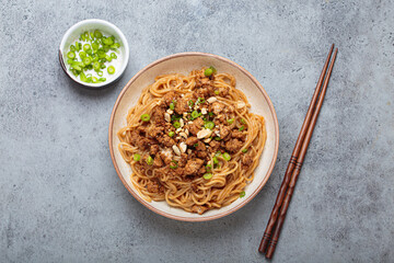 Dan dan noodles are being served with chopsticks and green onions in a bowl, showcasing the delicious flavors of sichuan cuisine