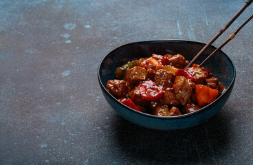 Delicious serving of sweet and sour pork is presented in a blue bowl, with chopsticks, Asian cuisine