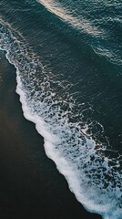 Gentle white sea foam washes black sand beach, creating soothing pattern. Ocean waves meet shore, bringing tranquility
