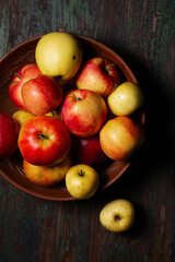 Juicy ripe apples in a large clay bowl on a wooden background