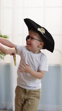 Toddler boy in pirate hat and eye patch attacks elder sister with toy sword playfully. Happy children siblings play duel running around room and making noise