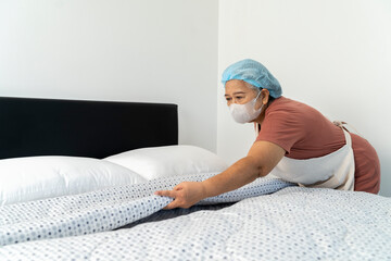 Senior housekeeper organizes the blankets and pillows on the bed in bedroom