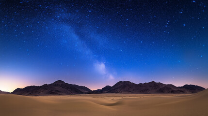A clear night sky filled with stars and the Milky Way shining over desert sand dunes and distant mountains