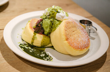 Japanese style sluffy souffle pancake dessert with green tea ice cream and cream served on a white plate on a wooden table
