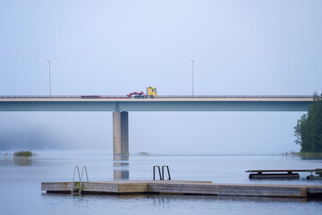 A truck crossing a foggy bridge over a lake