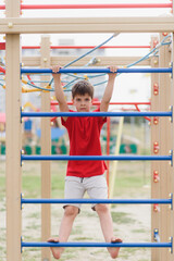 Obraz premium Happy boy playing and hanging on steel bar on playground. Children's exercises for health and concentration.