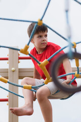 Happy boy playing and hanging on ropes on playground. Children's exercises for health and concentration