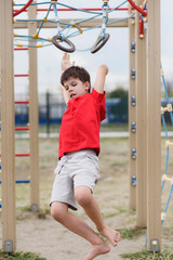 Happy boy playing and hanging on rings on playground. Kids exercises for health and concentration outdoors