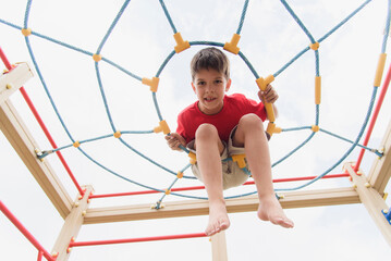 Happy boy playing and hanging on ropes on playground. Children's exercises for health and concentration