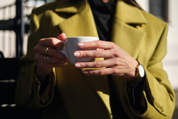 close-up hands holding a cup of coffee against the background of a street cafe with space for an inscription