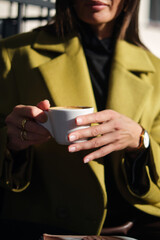 close-up hands holding a cup of coffee against the background of a street cafe with space for an inscription