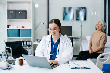 Young female doctor in white medical uniform using laptop and tablet talking video conference call at desk,Doctor sitting at desk and writing a prescription for her patient