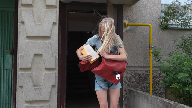 Slow motion view of angry teen girl leaves of the soviet apartment building and rushing to the school. Teenager late for school, puts her books in the backpack. Beautiful Caucasian girl.