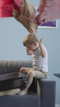 Naughty little children throw gathered clothes out of open suitcase in living room. Playful boy and girl have fun messing with apparel at home
