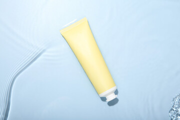 Cosmetic product. Tube with cream in water on light blue background, top view