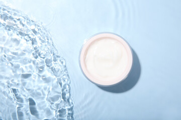 Cosmetic product. Jar with cream in water on light blue background, top view