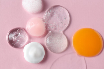 Smears of different cosmetic products on pink background, top view