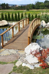 Beautiful wooden bridge over a pond, with plants and stones, on a sunny day.